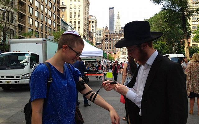Illustrative: A Chabad representative lays phylacteries on a passerby in New York’s Union Square on Friday, June 19, 2015 (Facebook)